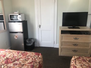 A bedroom with a TV, drawer, microwave, and refrigerator